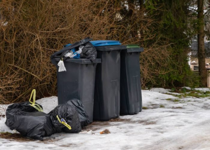 garbage bin full of trash on white snow in residential area in winter.